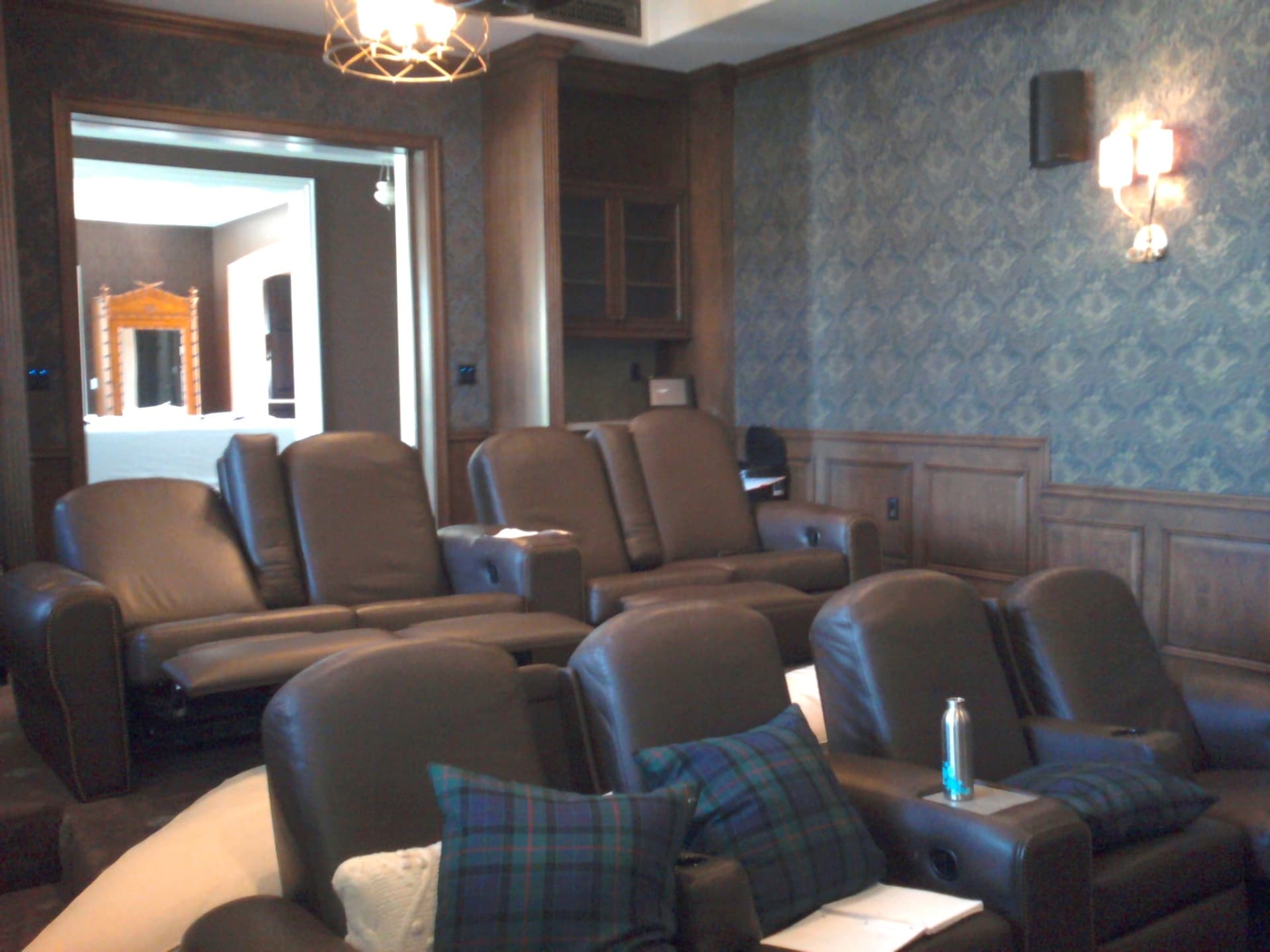 Multi-row leather theater seating with wall sconces and damask wallpaper in upscale media room