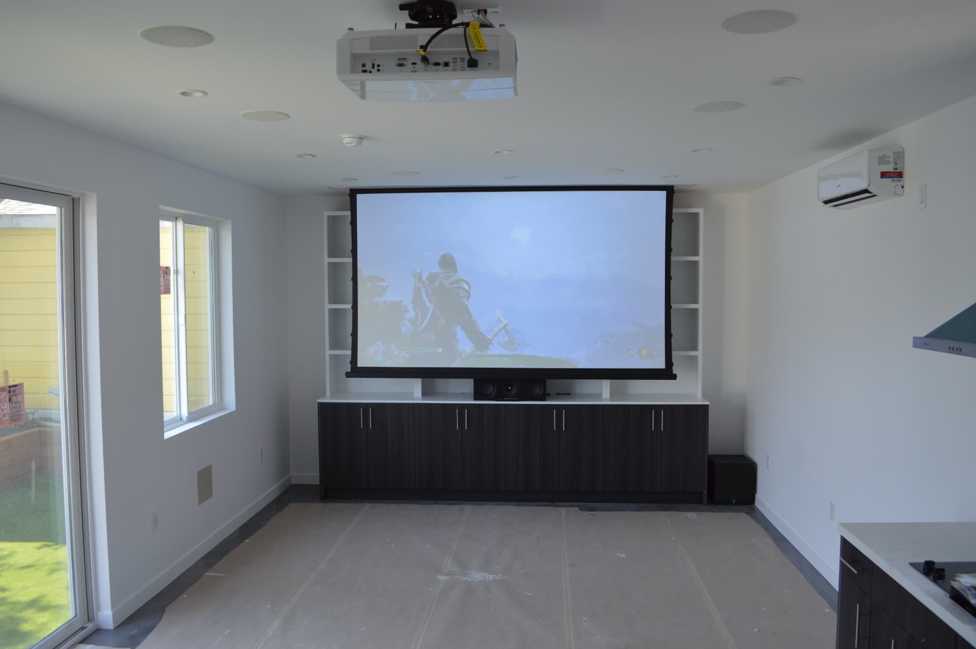 Bright media room with ceiling-mounted projector, motorized screen, and in-ceiling surround speakers