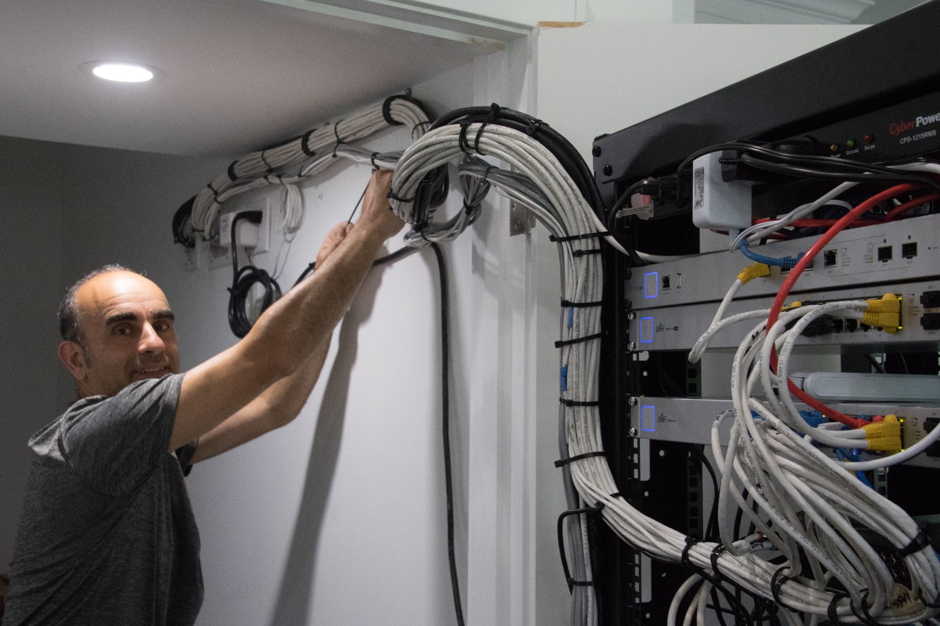 Technician organizing a large bundle of white network cables along the wall into a structured rack