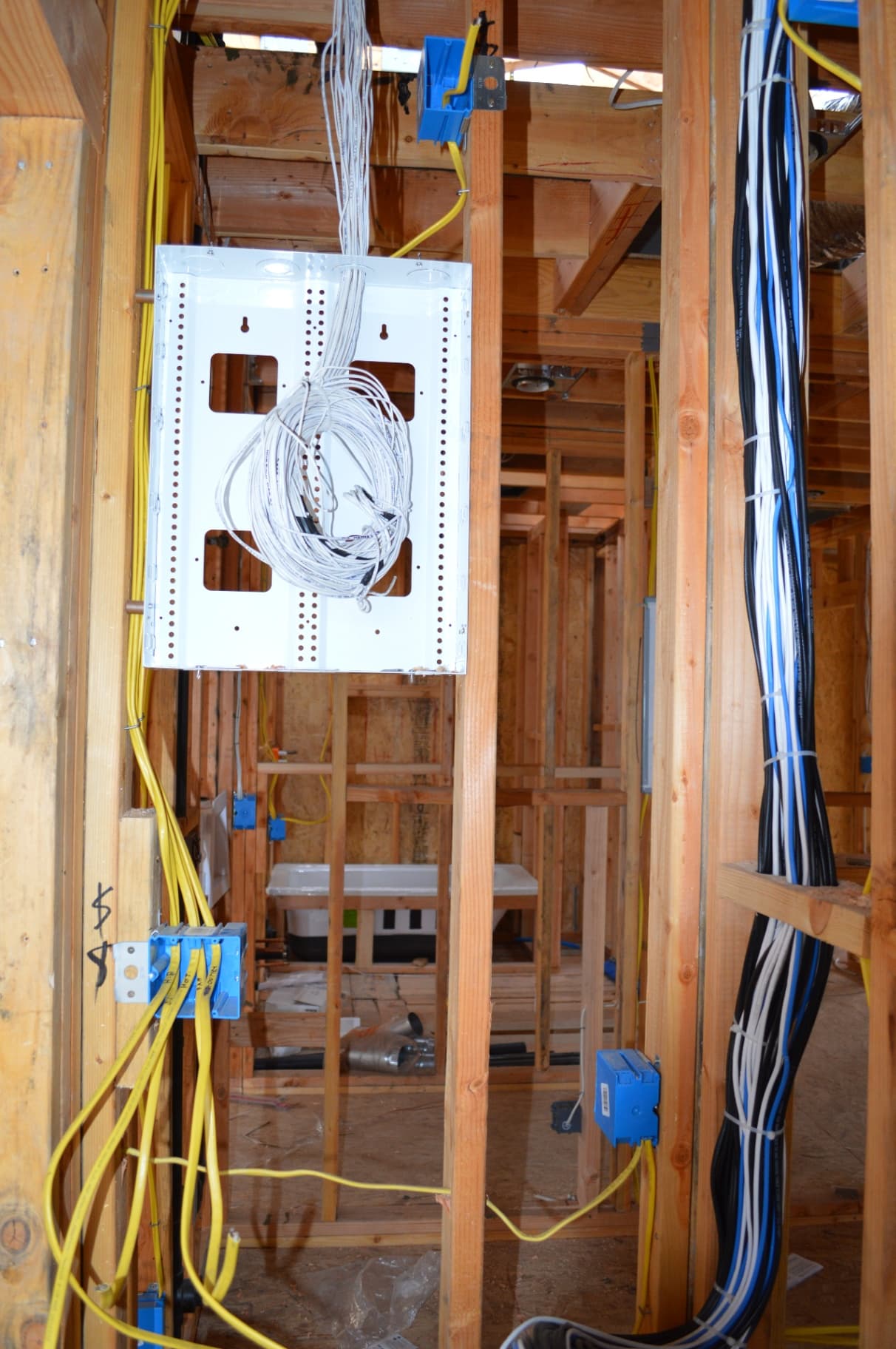 New construction framing with low-voltage panel and vertical bundle of blue, black, and white cables
