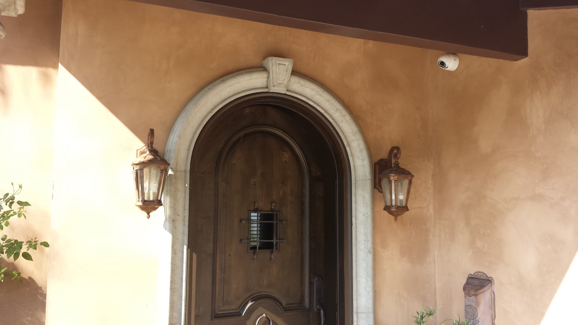 Spanish-style front entry with arched wooden door and discreet security camera above doorway