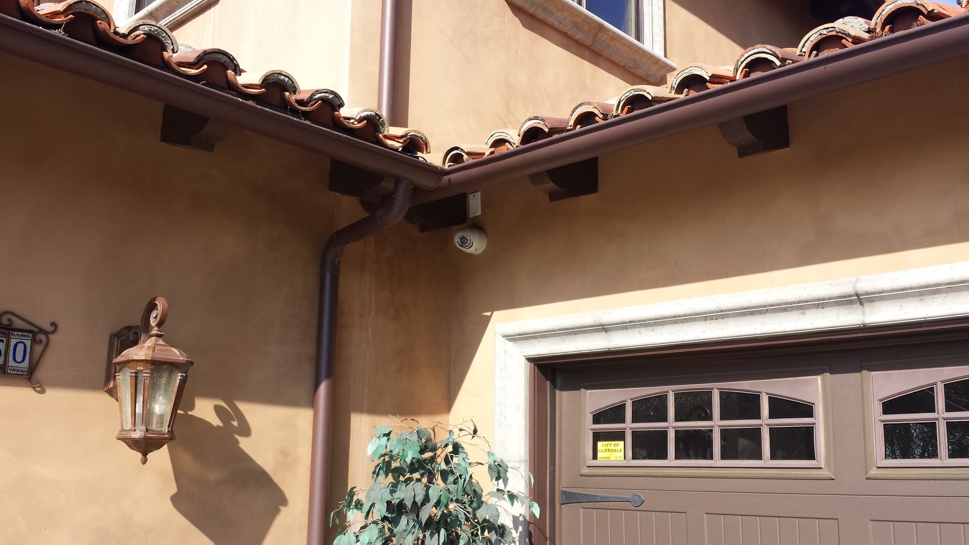 Driveway and garage area with security camera mounted under roof eave for vehicle coverage