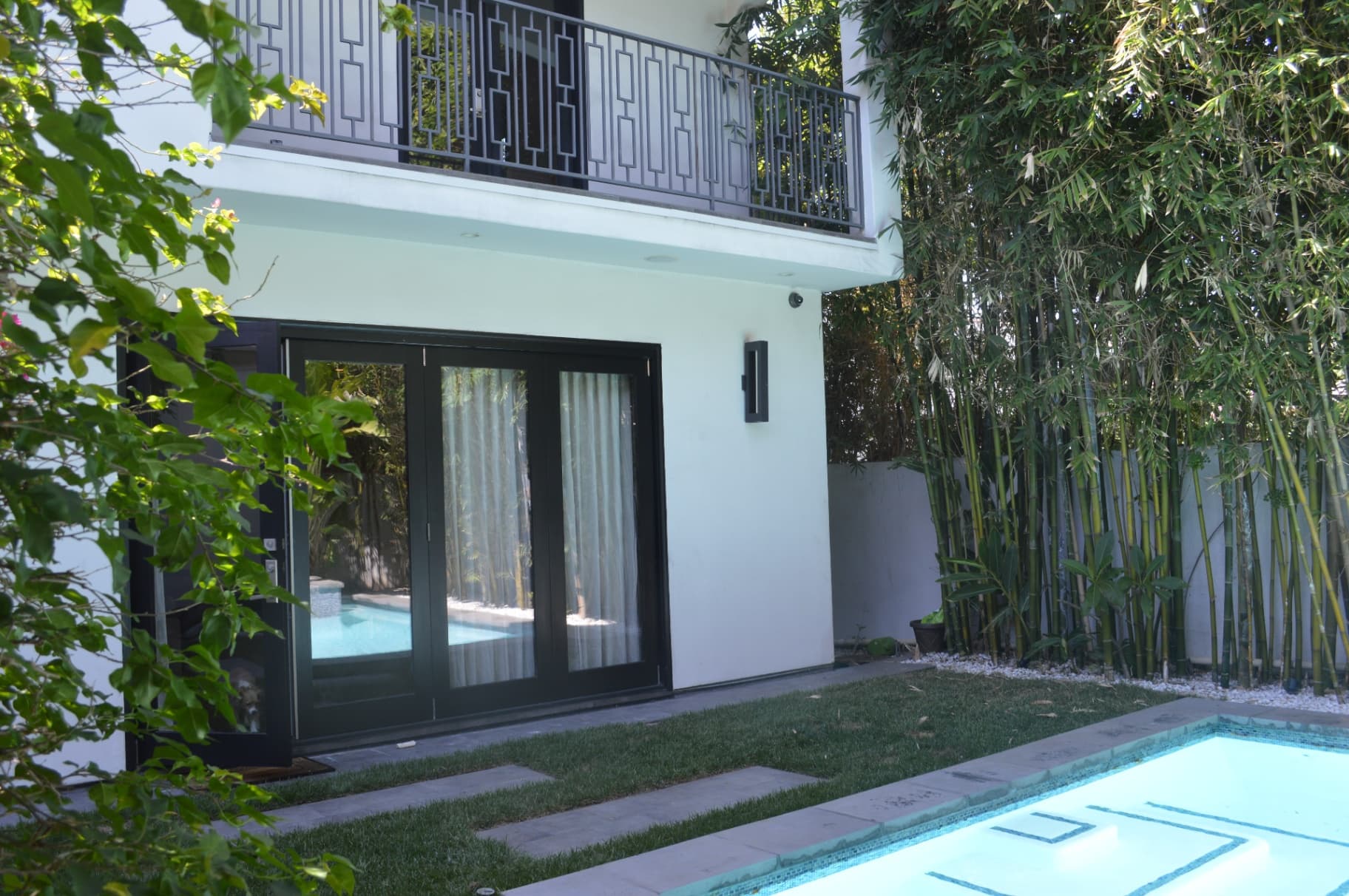 Modern backyard with pool and security camera watching large glass doors to patio