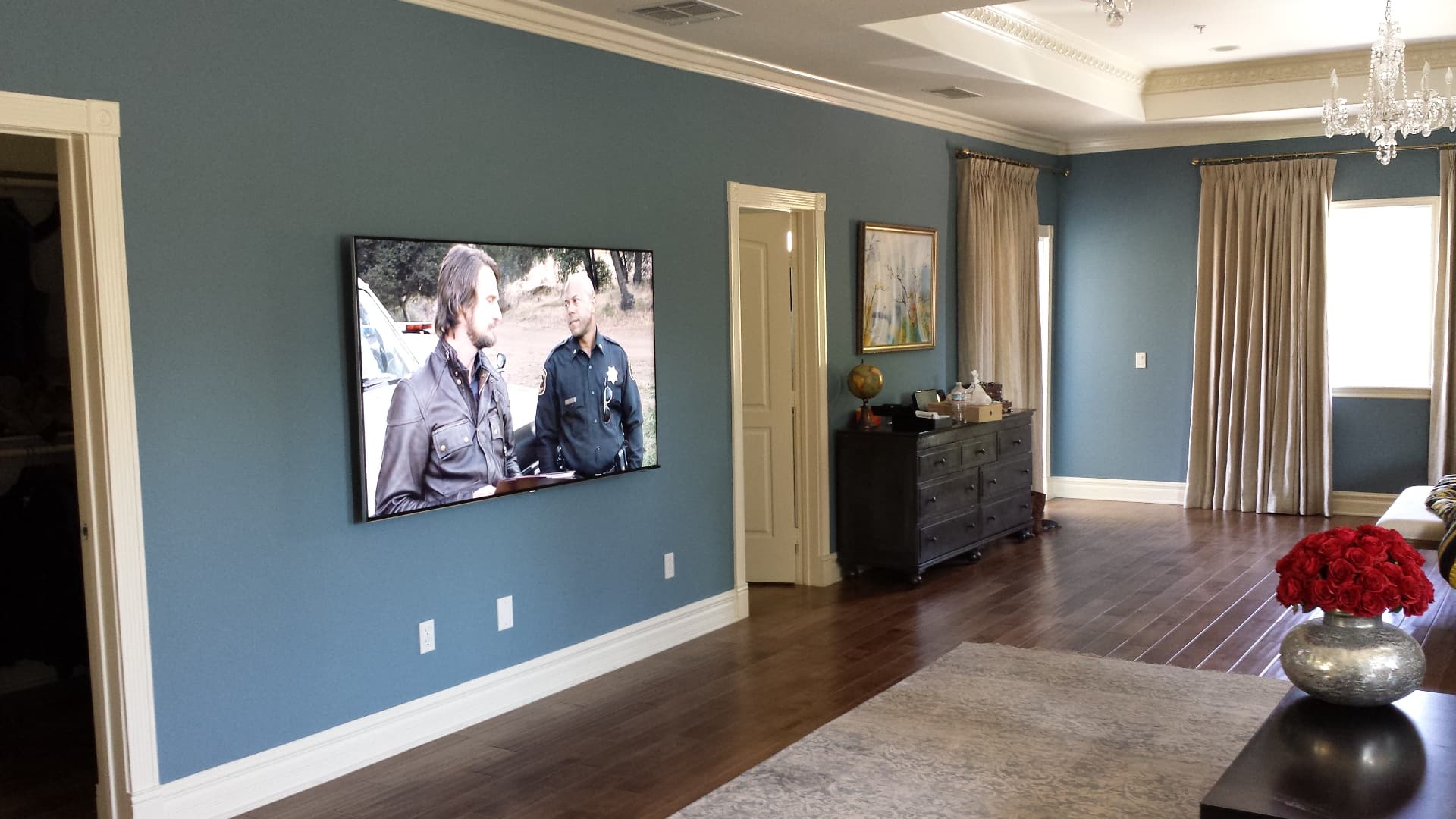 Large flat-screen TV mounted on blue accent wall in elegant living room with hardwood floors