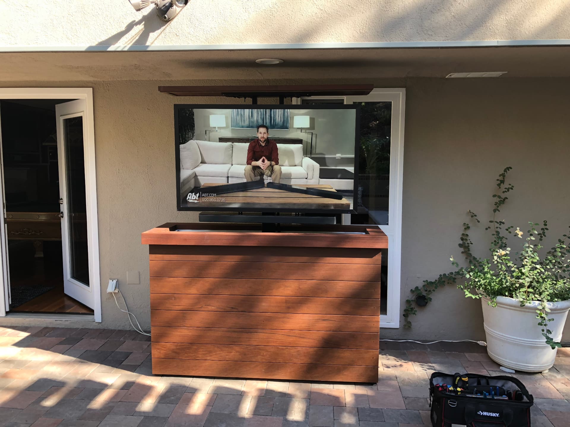 Outdoor TV on motorized lift in wooden cabinet on patio
