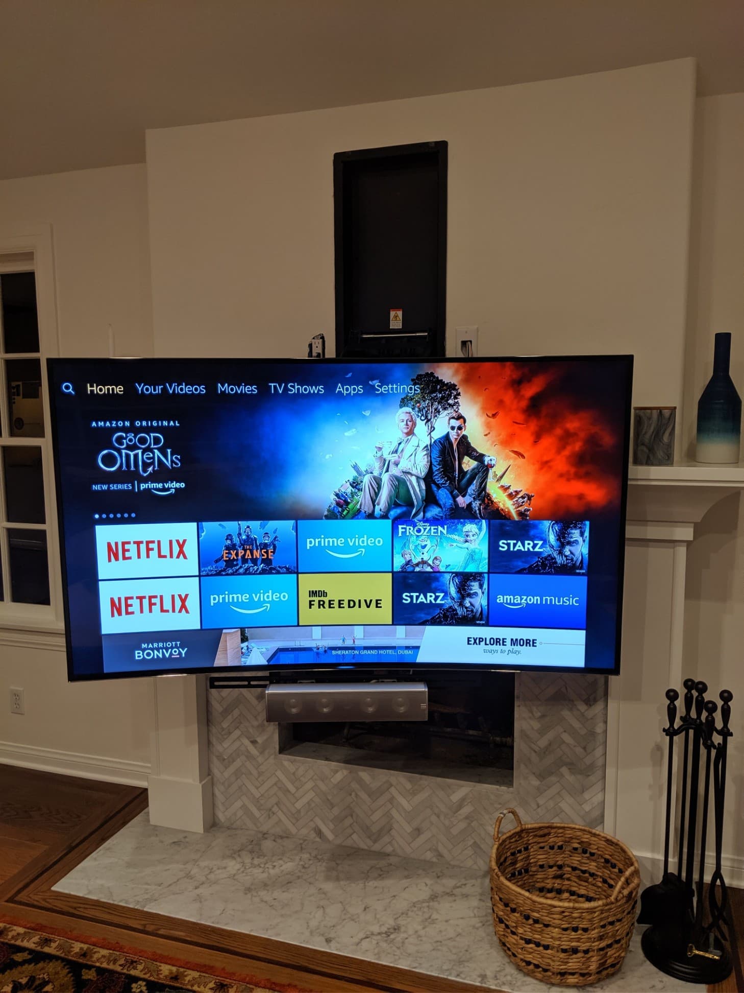 Curved TV mounted above white herringbone-tile fireplace displaying streaming apps in cozy living room