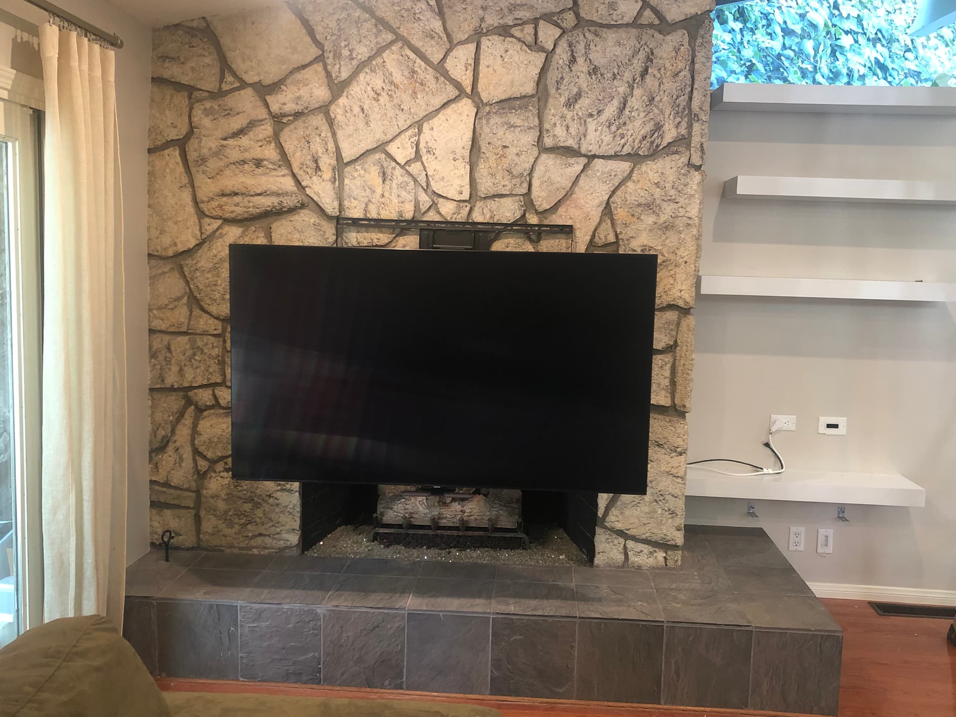 Large TV extended on articulating mount in front of natural stone fireplace, demonstrating flexible viewing angles