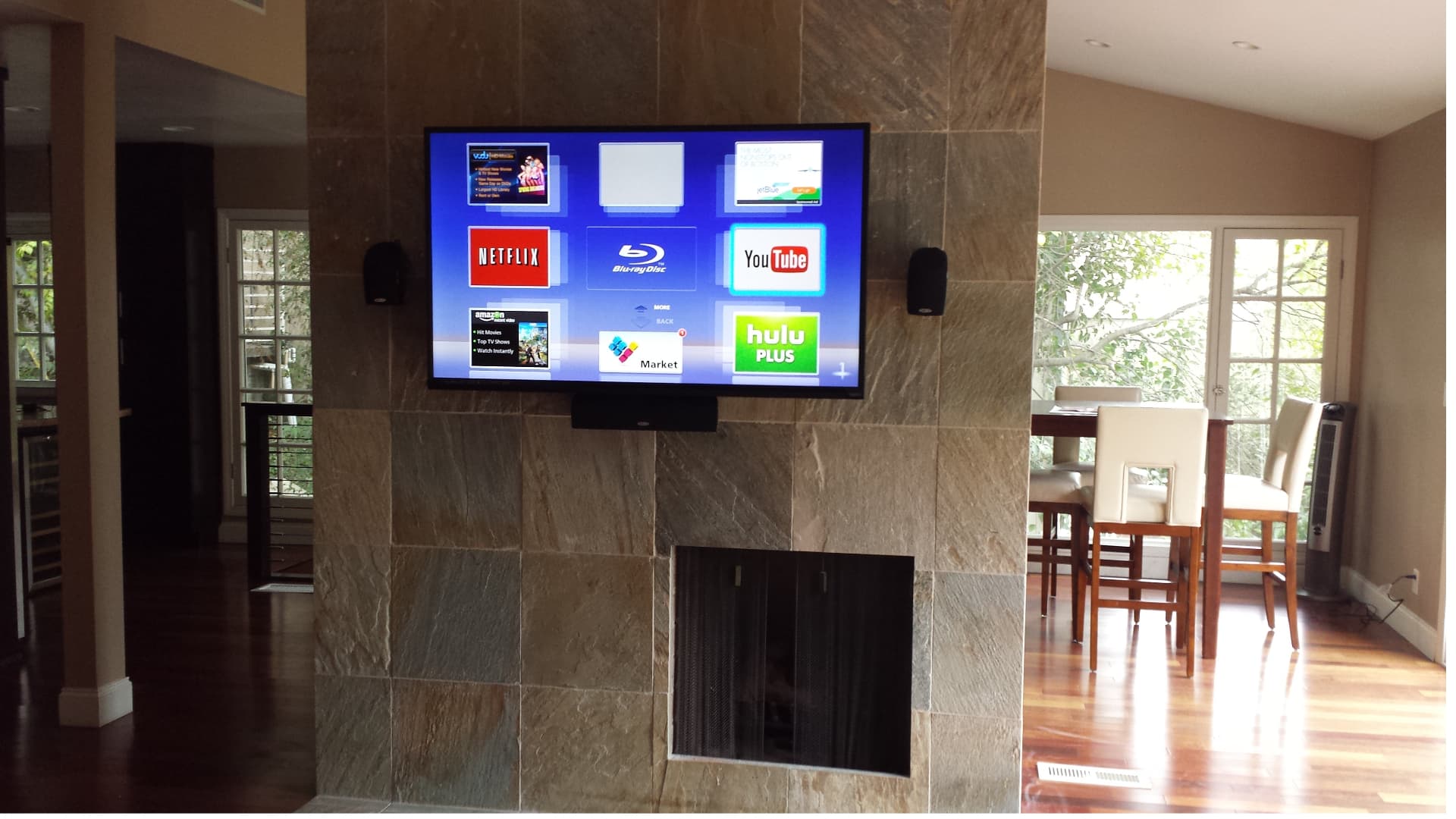 TV mounted above stone fireplace with streaming apps displayed and surround speakers