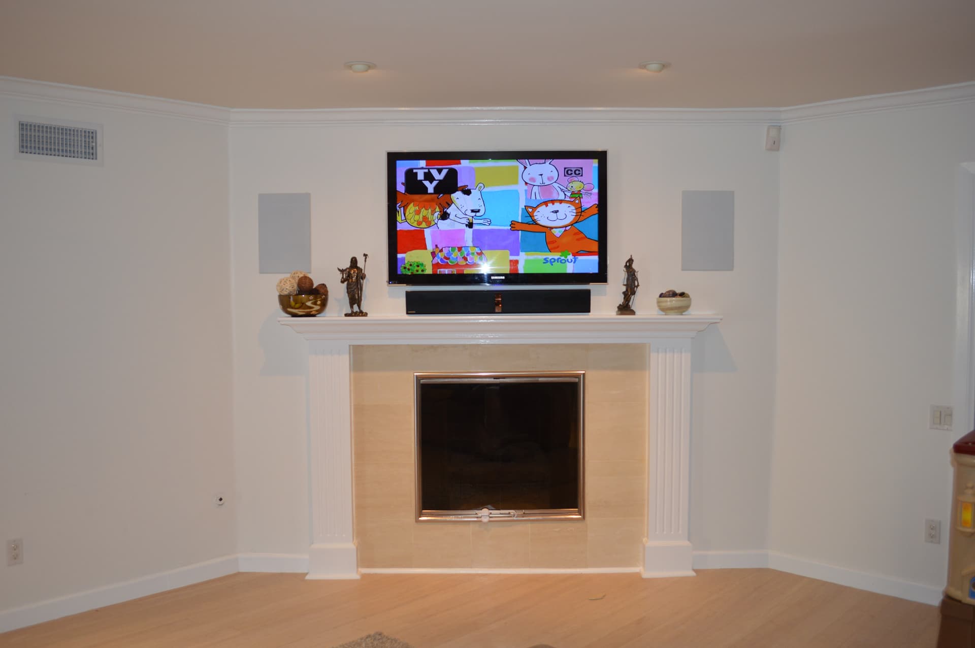 TV above traditional fireplace with in-wall speakers and soundbar on mantel